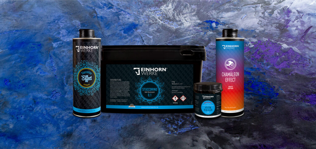 Einhornwerke-Produkte zur Wandgestaltung stehen vor einer künstlerisch gestalteten Wand mit blauen und violetten Akzenten.