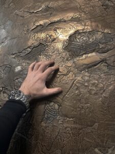 Eine Hand berührt eine kunstvoll strukturierte Wand mit edler Metalloptik, ideal für kreative Wandgestaltung im Wohnzimmer.